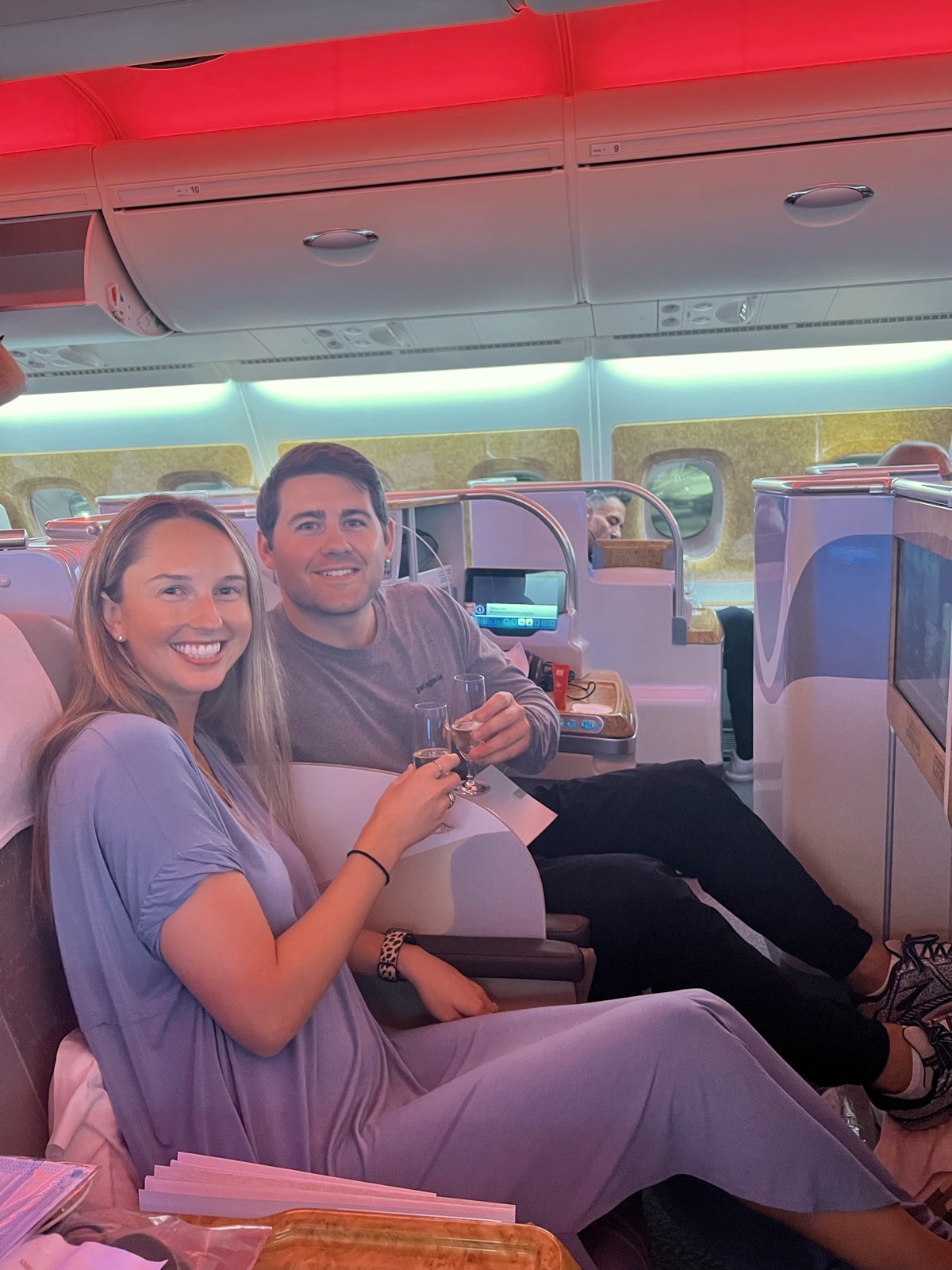 Mike and Christie seated side by side, smiling and raising their glasses in a spacious premium cabin