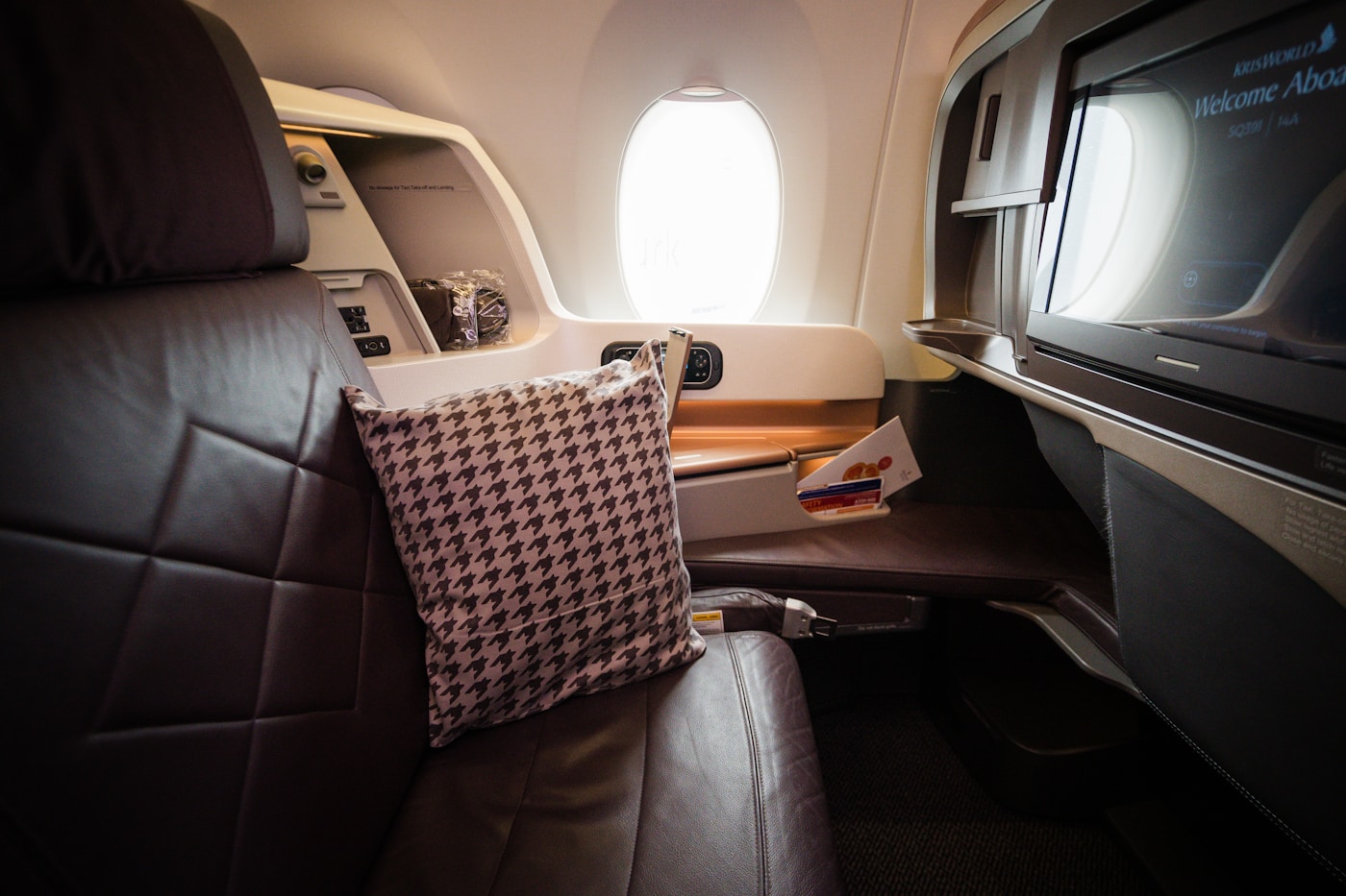An empty Singapore Airlines business-class seat beside the window, with a wide leather seat and individual screen